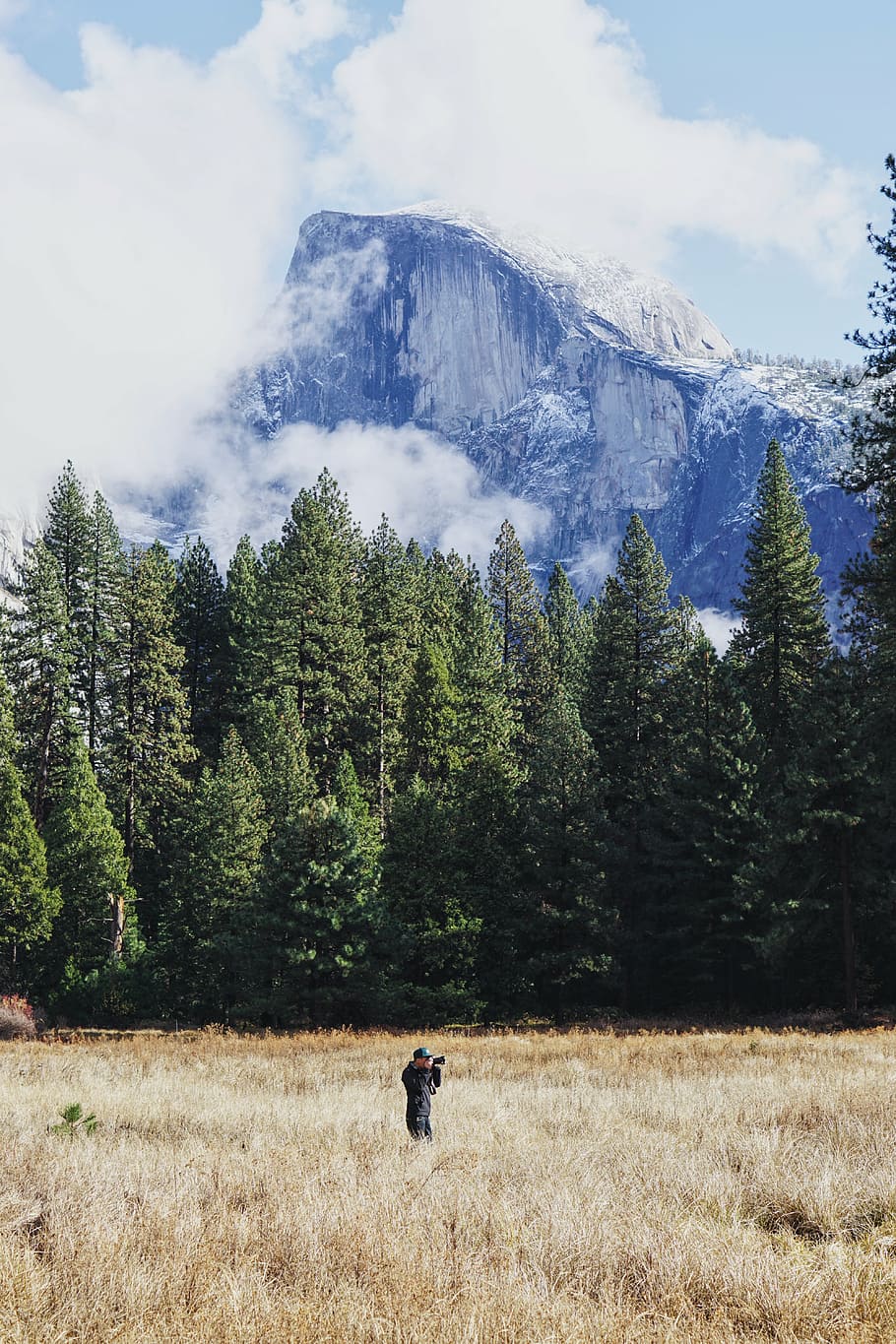 man taking photo while standing on withered grass field under snow capped mountain HD wallpaper