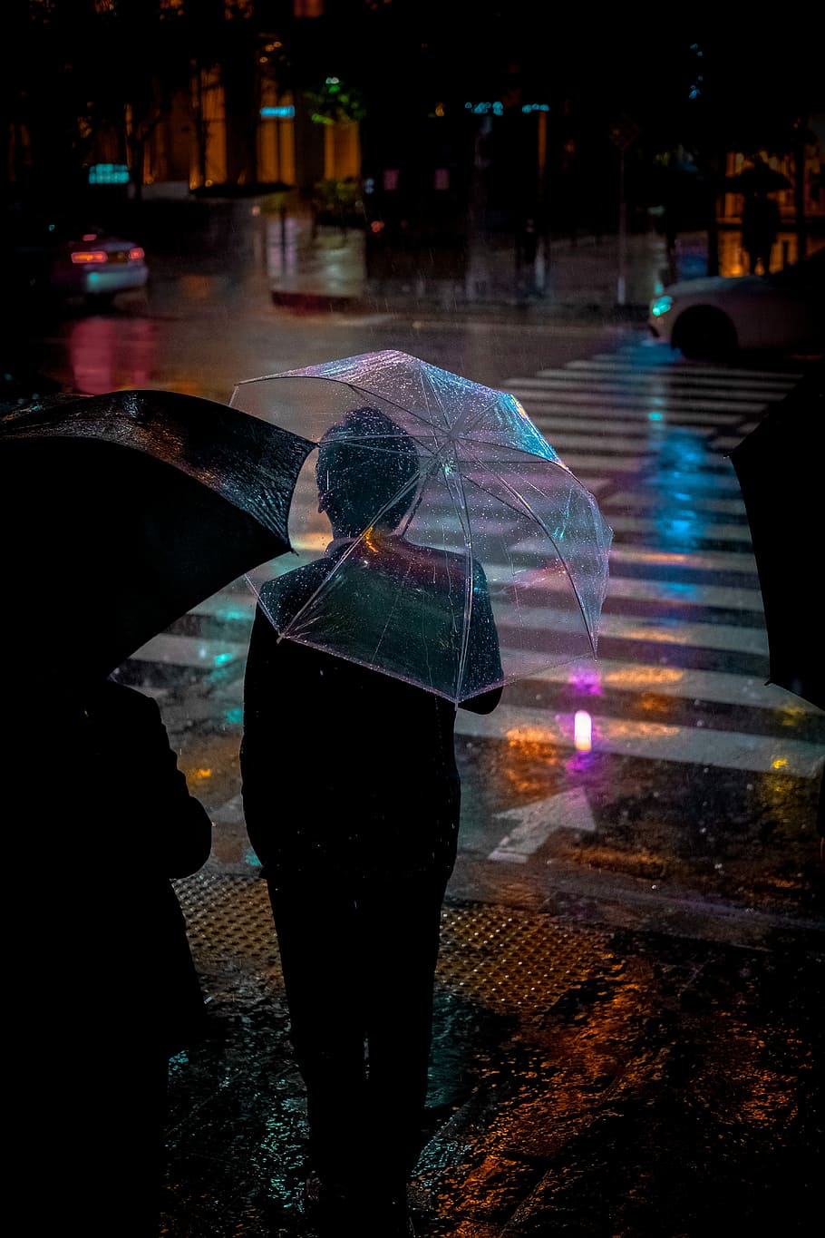 man wearing black suit jacket holding clear umbrella in front of pedestrian lane, person standing near pedestrian lane while carrying an umbrella during night