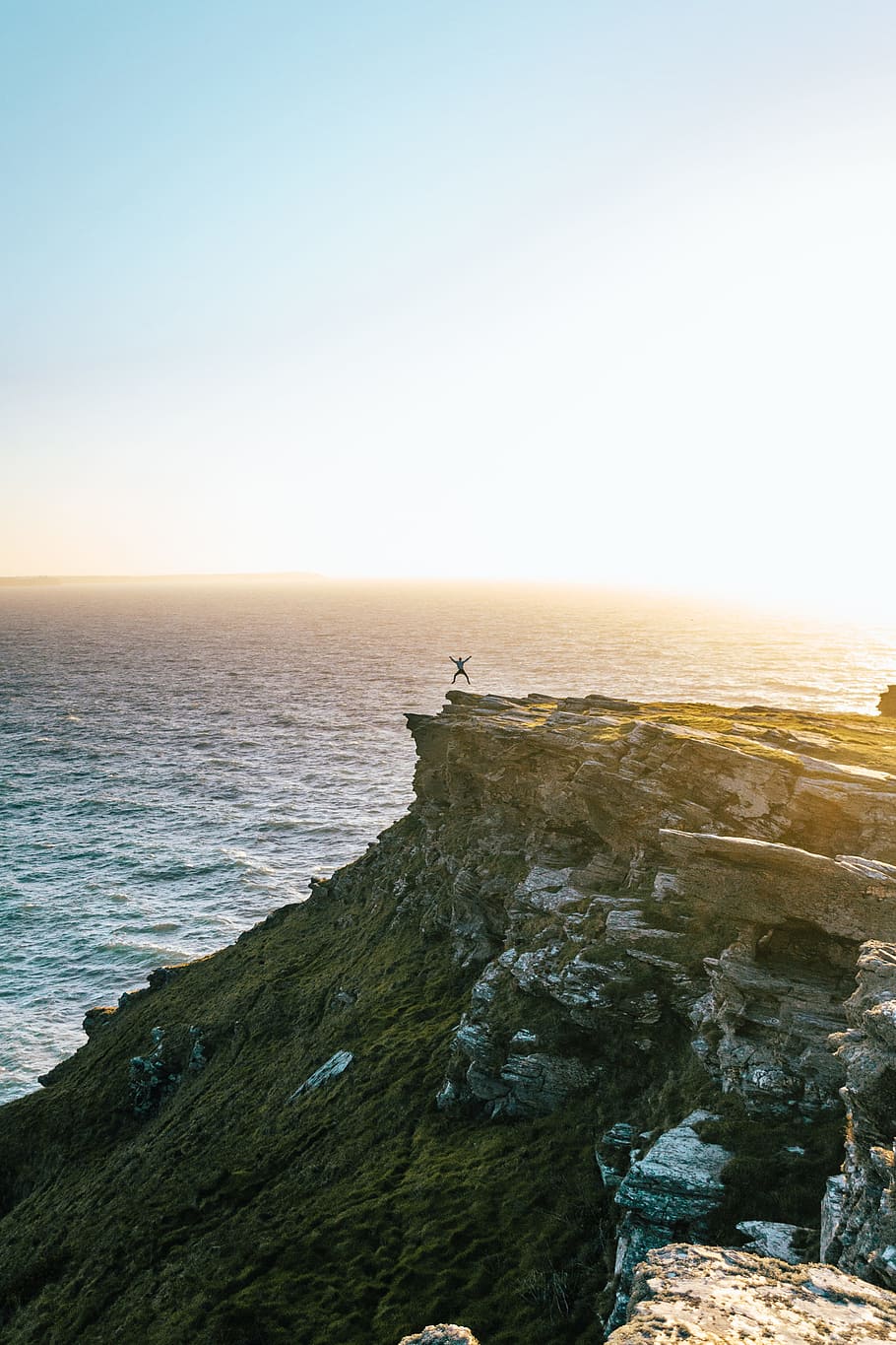 man jumping on cliff, person jumping on cliff near body of water during golden hour HD wallpaper