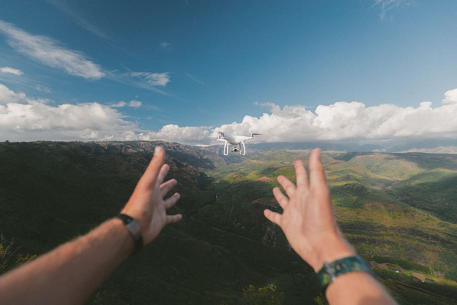 person pointing both hands on white drone during daytime, quadcopter drone in front of person and mountains in background HD wallpaper