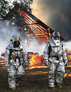 two fireman walking on the grass with burning fire house at the back HD wallpaper