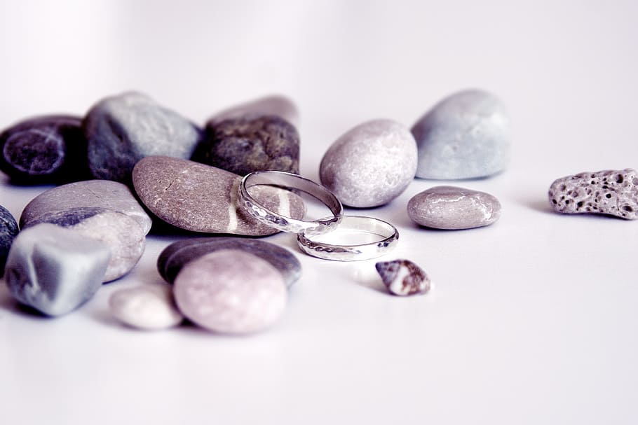 pair of silver-colored wedding band on top of white surface beside gray stone, HD wallpaper