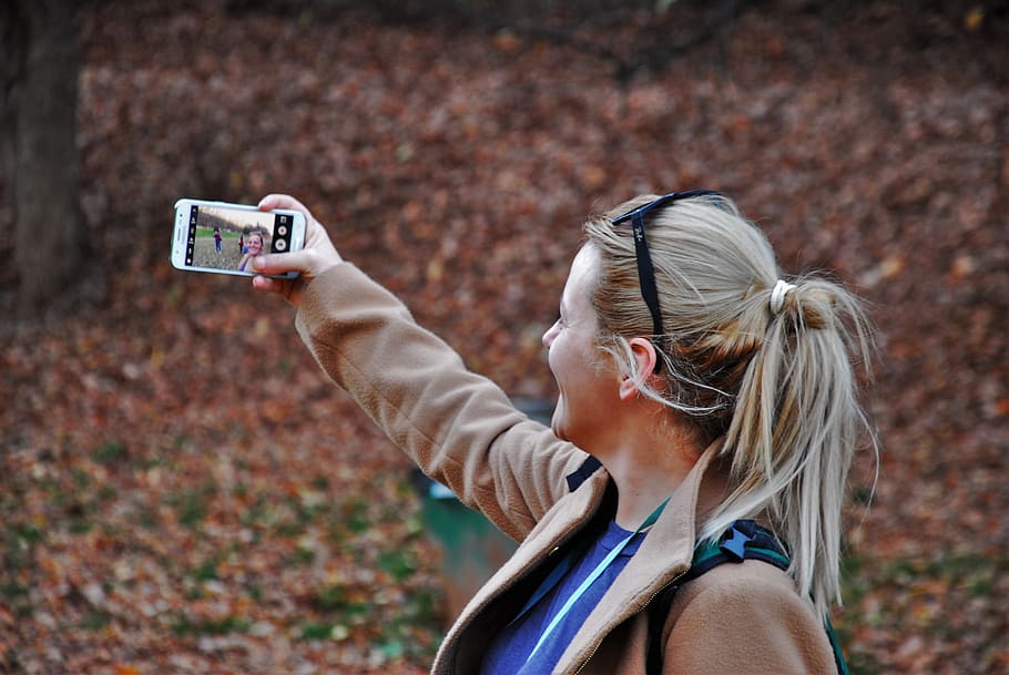 photo of a woman wearing brown jacket holding white Android smartphone, HD wallpaper