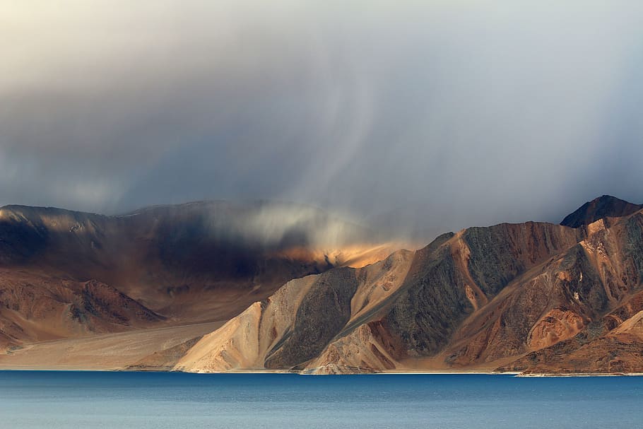 body of water and brown mountain under white sky at daytime, brown mountain near ocean under white sky HD wallpaper