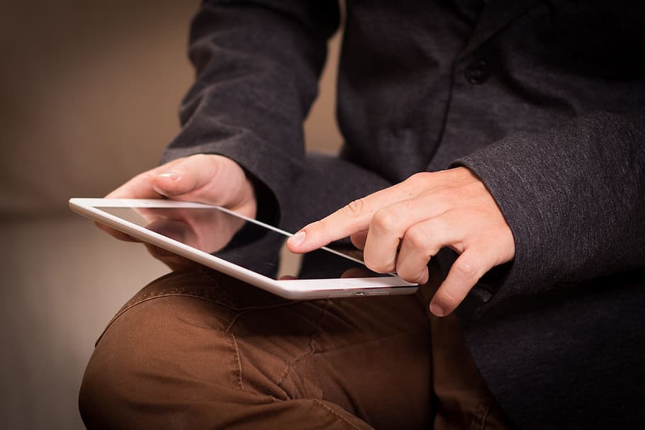 person wearing black dress shirt and brown pants holding white ipad HD wallpaper