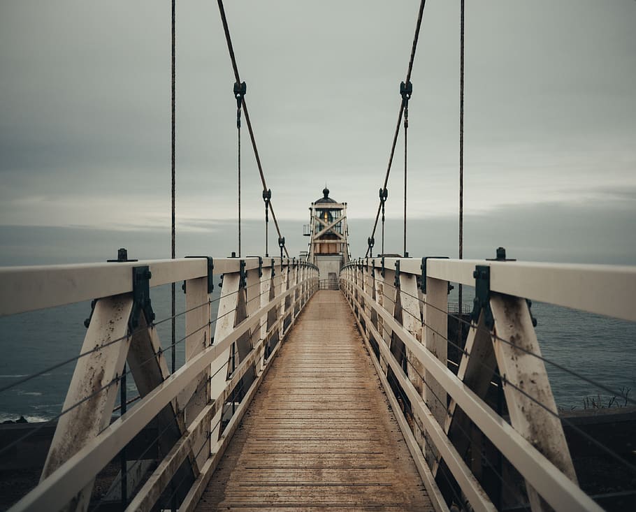 brown wooden lighthouse with bridge near seashore during daytime, gray steel bridge during cloudy day HD wallpaper