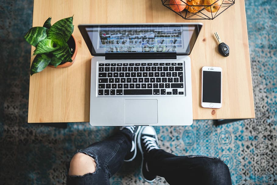 Woman in ripped jeans and black sneakers with a silver laptop on a wooden table HD wallpaper