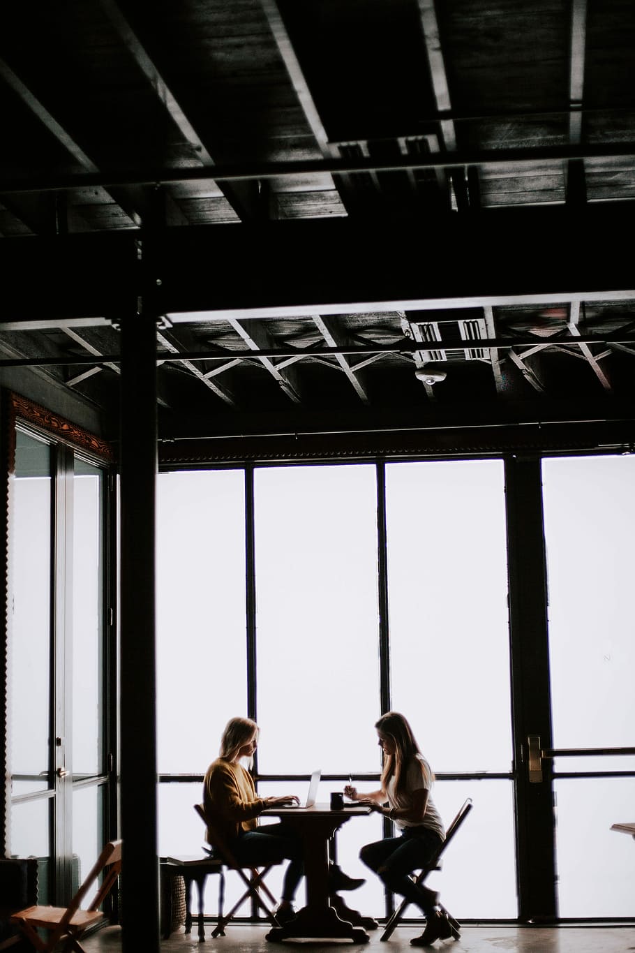 photo of two women facing each other sitting in front of table near glass wall, two women sitting inside shop HD wallpaper