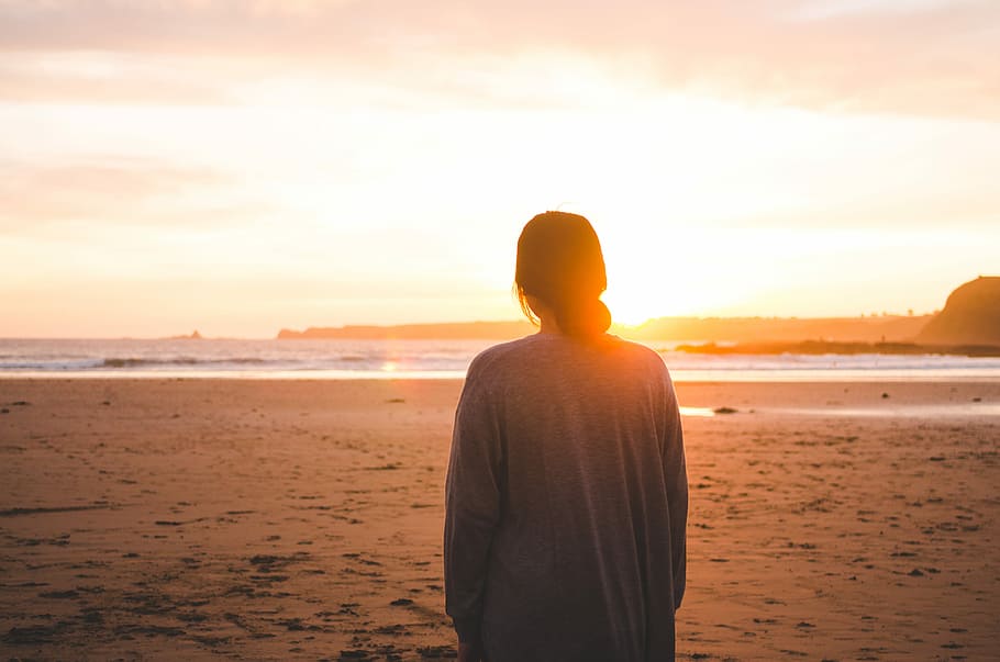 woman standing on sand and facing at seashore, woman looking at sun during golden hour HD wallpaper