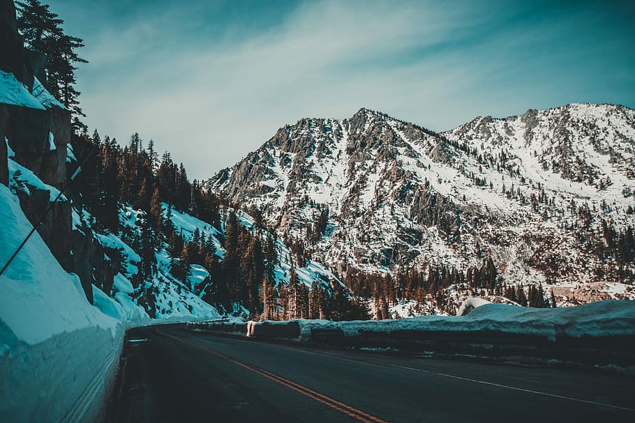 snowy mountain during daytime, asphalt road near gray mountain under gray sky HD wallpaper
