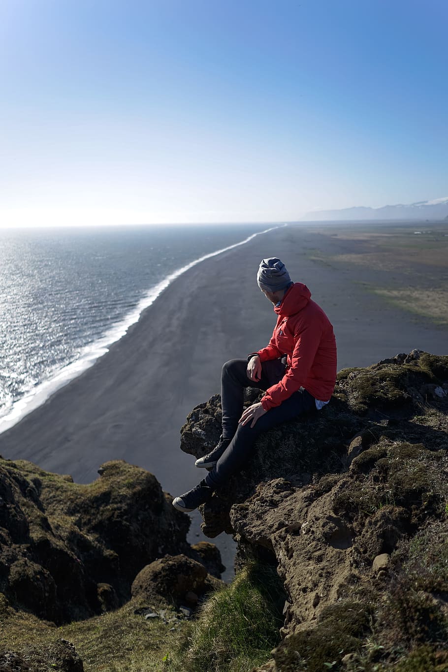 man sitting on mountain cliff near body of water, man sitting of brown mount cliff HD wallpaper