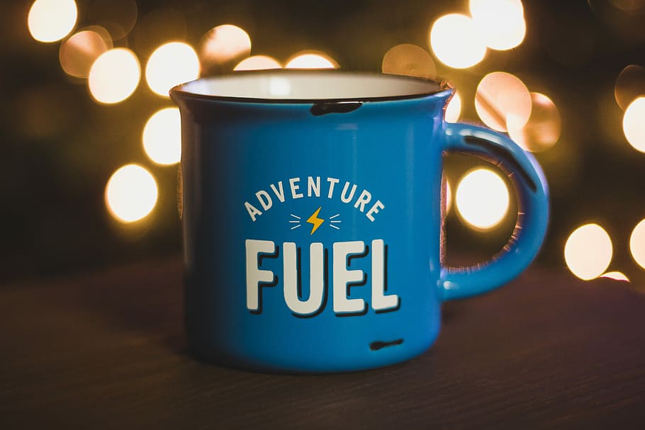 bokeh photography of blue ceramic mug on brown surface, blue Adventure fuel-printed cup