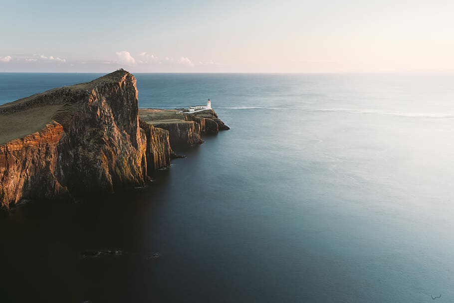 brown mountain cliff beside of blue ocean aerial photography, brown island and sea under cloudy sky