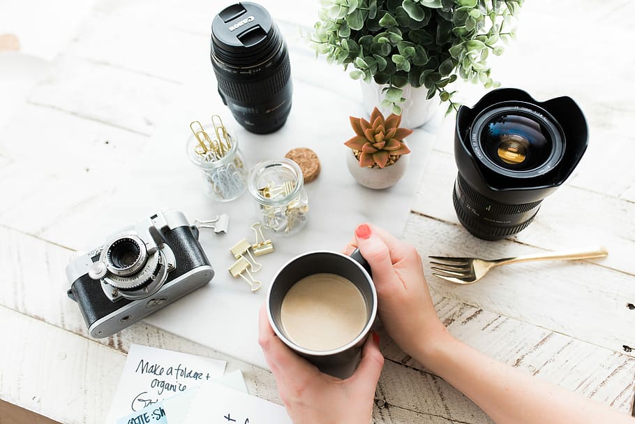 person holding black ceramic coffee mug beside black DSLR camera, person holding black mug filled with coffee HD wallpaper
