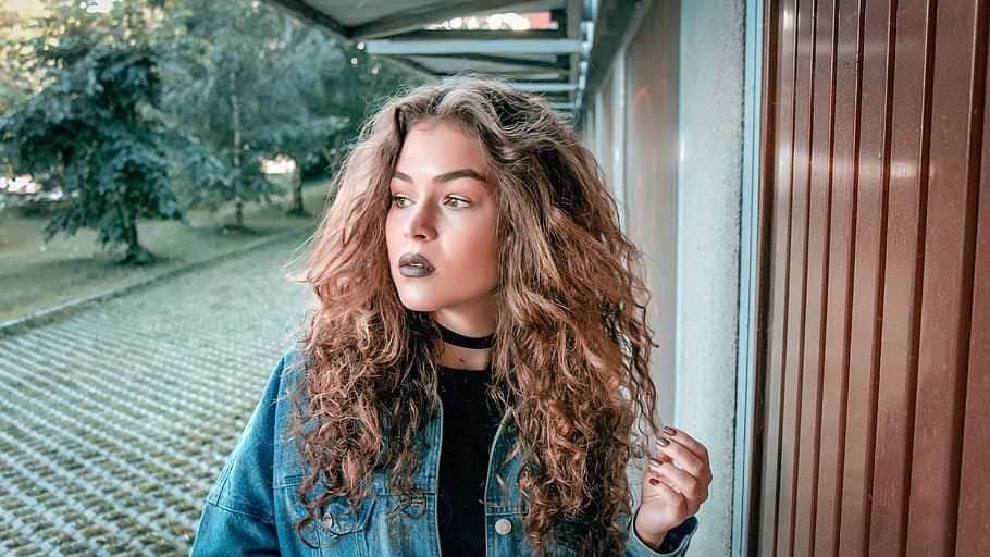 woman wearing blue denim jacket holding her curly hair, beautiful