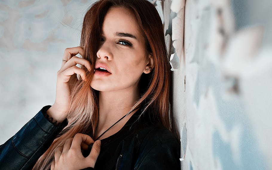 woman wearing black leather jacket while leaning on wall, young