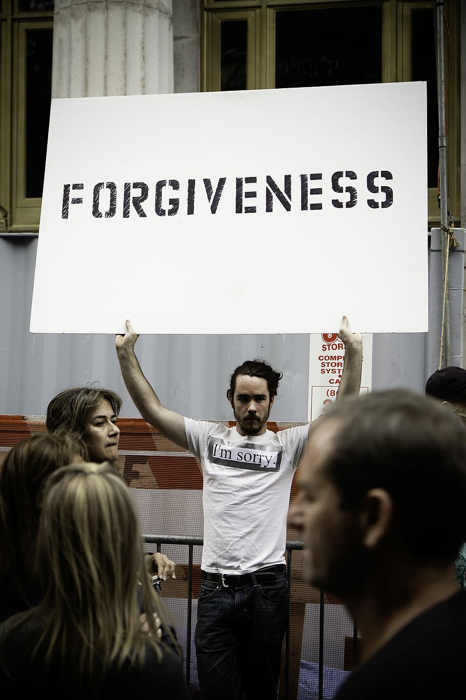 person holding Forgiveness poster, man in white crew-neck shirt holding forgiveness board standing near people HD wallpaper