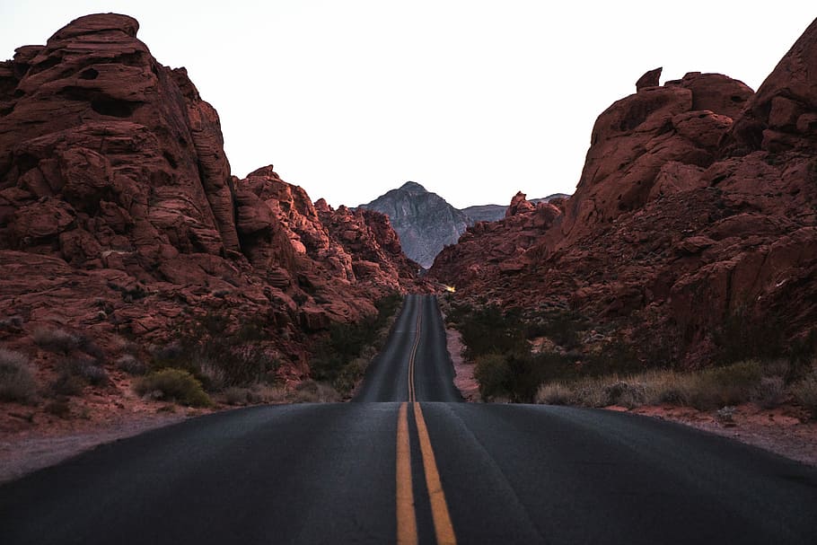 black and yellow concrete road beside brown rocky hills, black asphalt road during daytime HD wallpaper