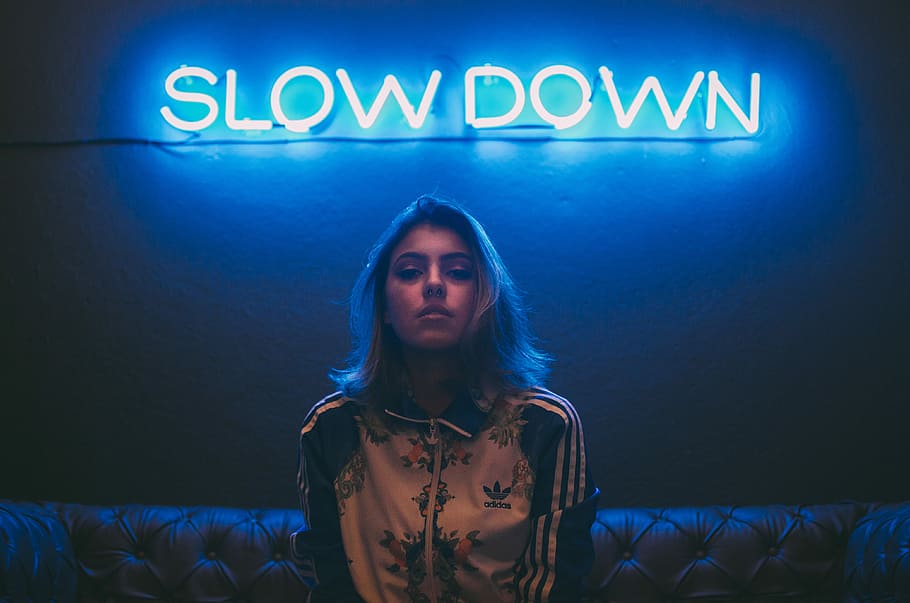 woman sitting on brown sofa under slow down neon signage, woman wearing adidas jacket sitting on sofa HD wallpaper