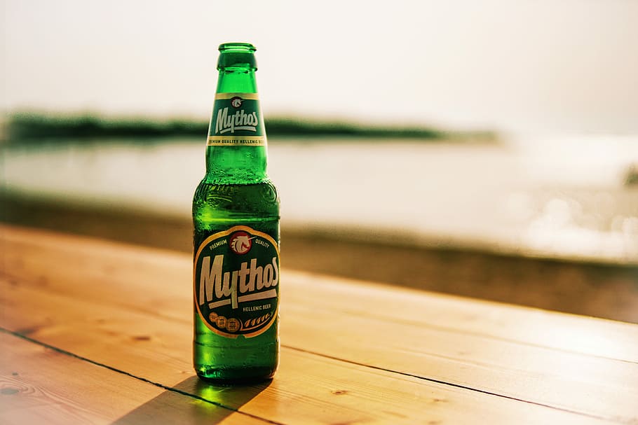 Mythos beer bottle on wooden table near beach, photo of green Mythos labeled bottle HD wallpaper