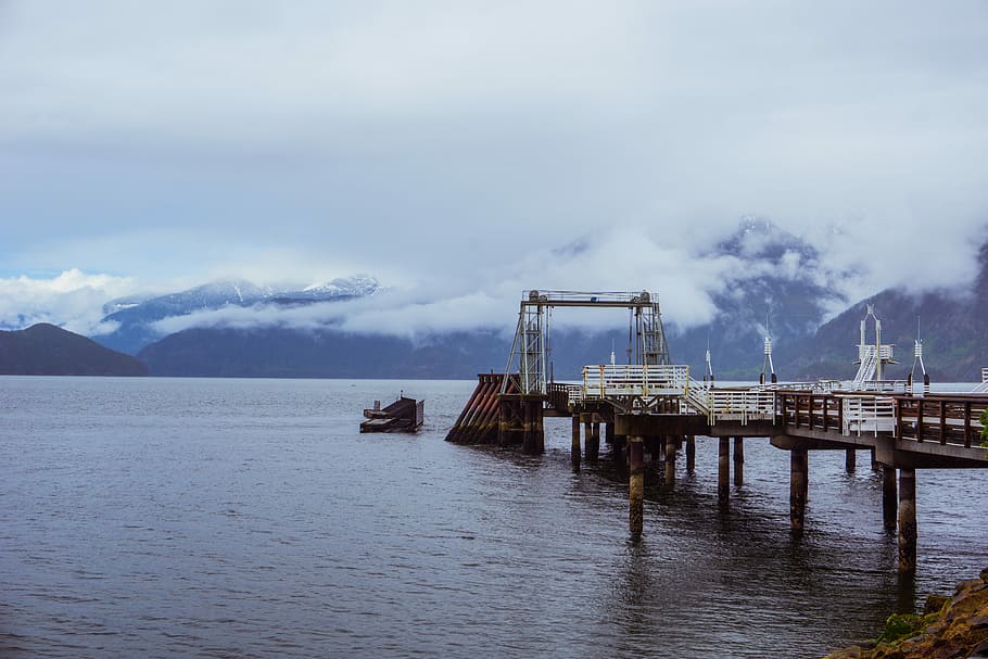 body of water under white clouds, dock on body of water with mountains in the background HD wallpaper