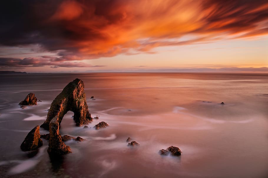 landscape photo of cliff, orange clouds calm sea during sunset