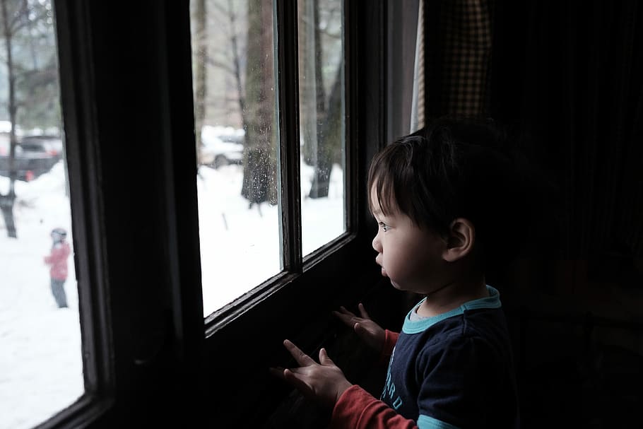 toddler boy standing near window during daytime, boy wearing blue top looking outside window HD wallpaper