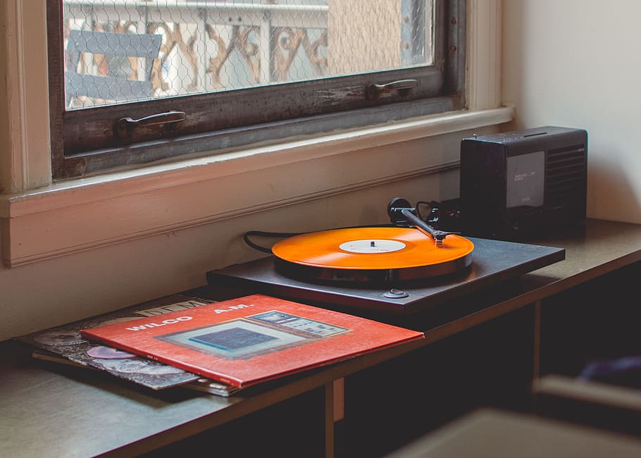gray turntable playing, black and orange vinyl player beside clear glass window