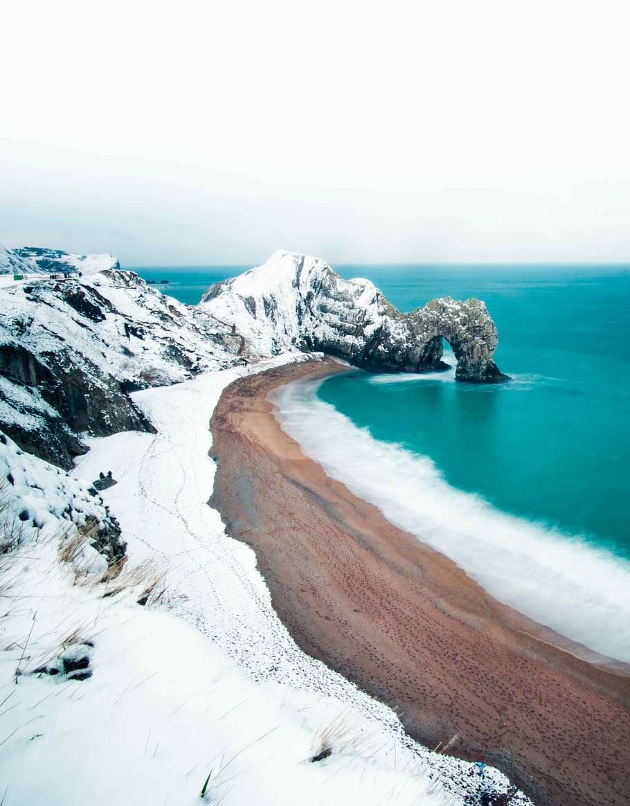 rock formation mountain covered by snow near sea, seashore during daytime