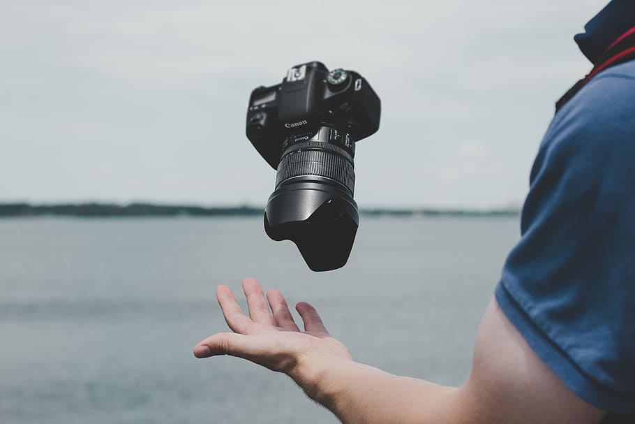 black Canon DSLR camera, person wearing blue shirt near body of water under cloudy sky during daytime HD wallpaper