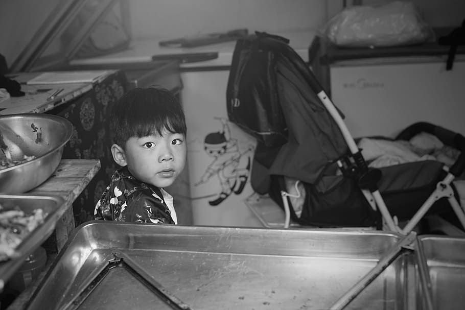 boy sitting in kitchen, grayscale photo of boy sitting near stroller