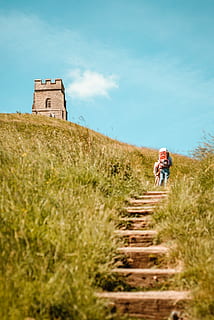 two person walks on hills near concrete stucture, low angle photo of person walking toward to tower at daytime HD wallpaper