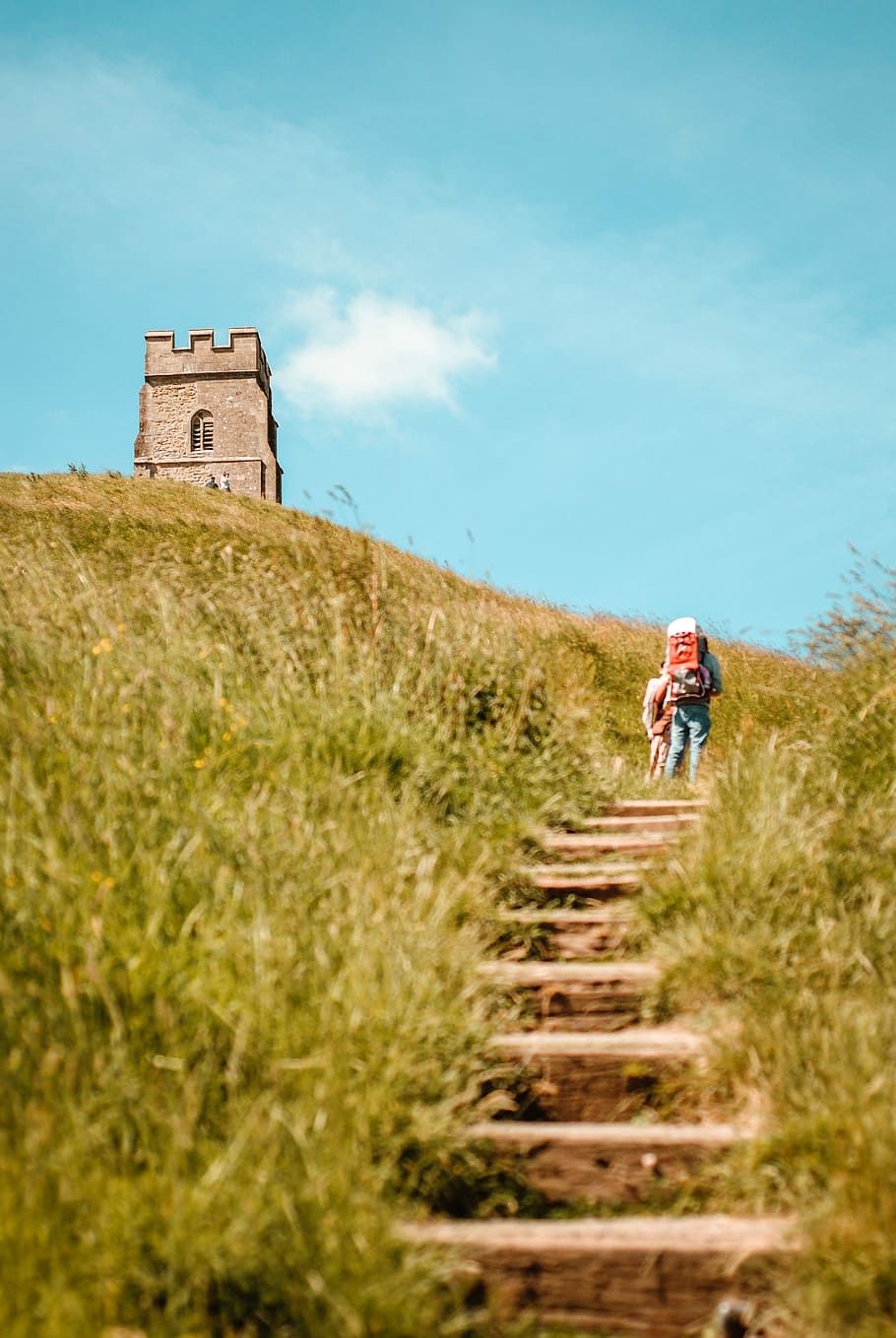 two person walks on hills near concrete stucture, low angle photo of person walking toward to tower at daytime HD wallpaper