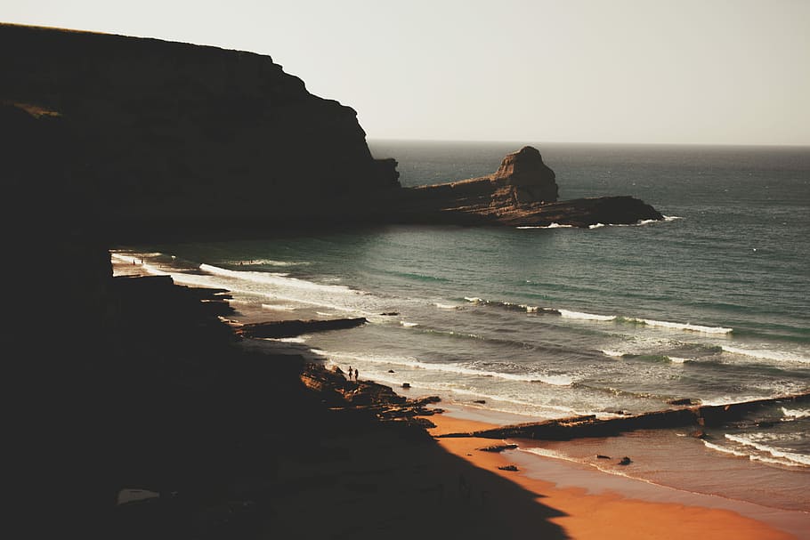 aerial photography of sea stack under gray sky, aerial photography of ocean waves on seashore at daytime HD wallpaper