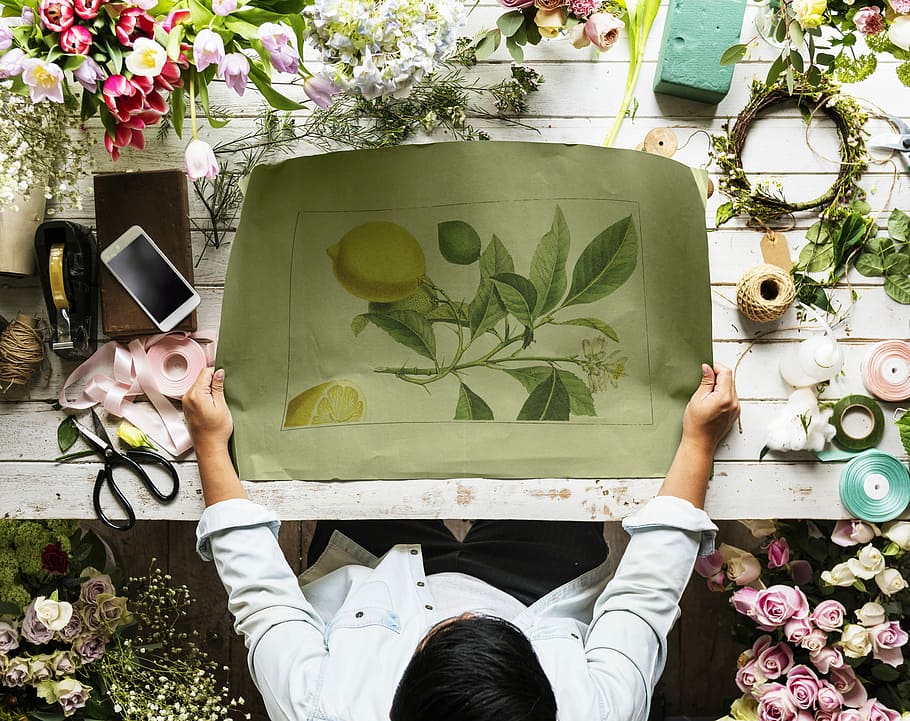 person holding yellow lemons painting on white wooden table with assorted flowers HD wallpaper