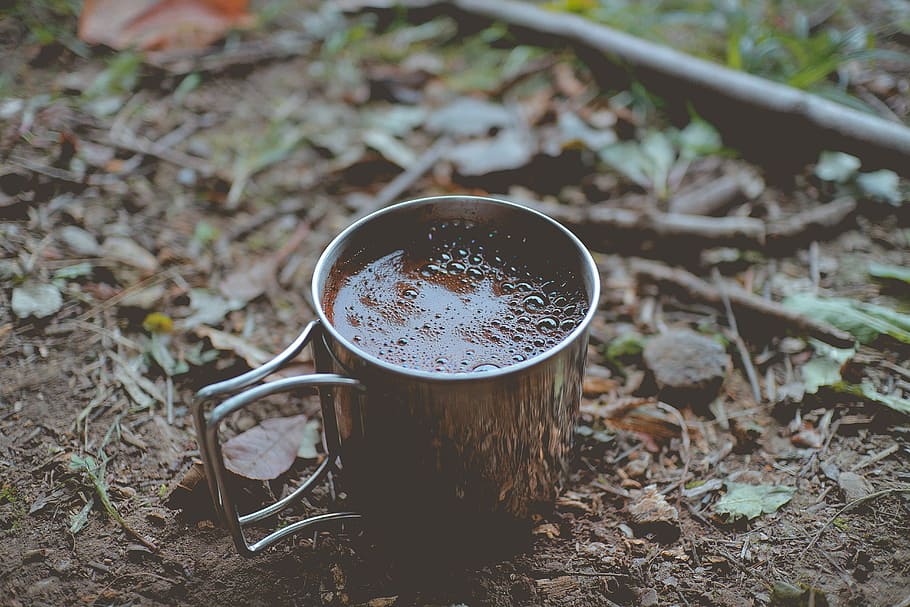 silver coffee mug on ground, filled brown mug on brown soil, cup