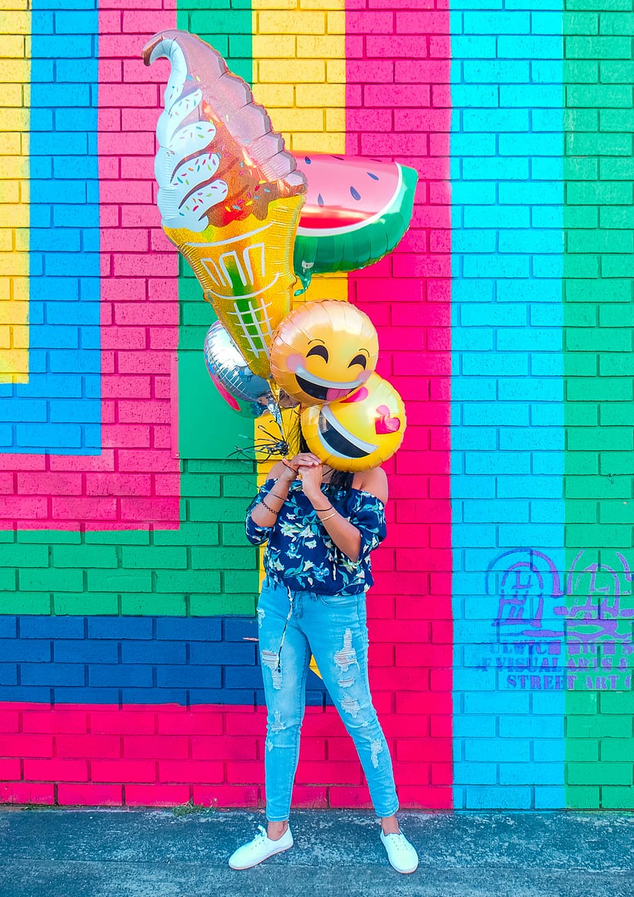 woman covering face with assorted ballons, woman holding helium balloons during daytime