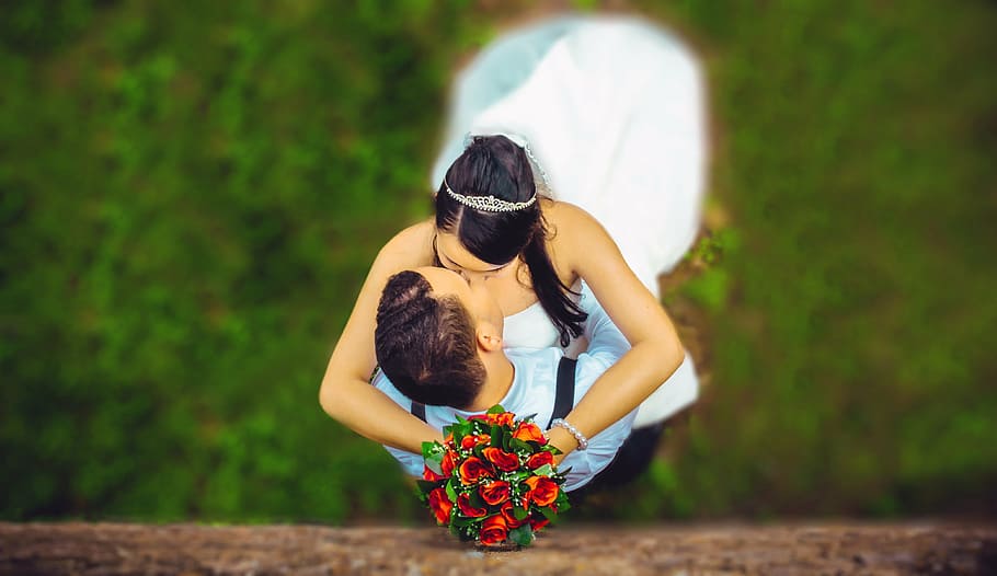 woman holding red rose bouquet while kissing man, wedding, grooms