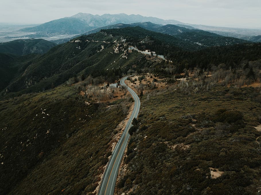 aerial view of road through mountains, aerial photography of road surrounded by trees at daytime HD wallpaper