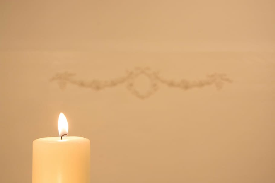lighted white pillar candle near wall with hanged decor, bright HD wallpaper