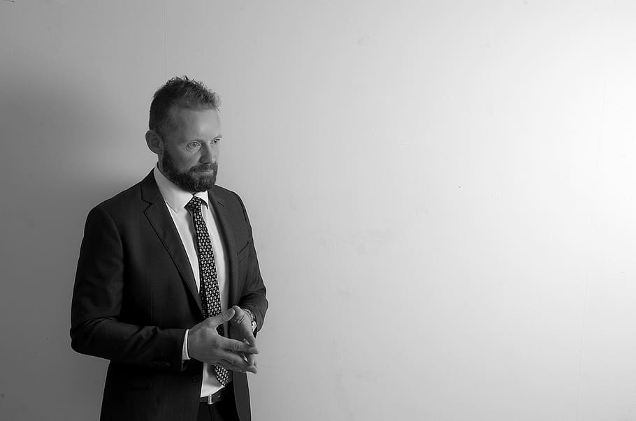 man standing near white surface, portrait, beard, suit, black and white HD wallpaper
