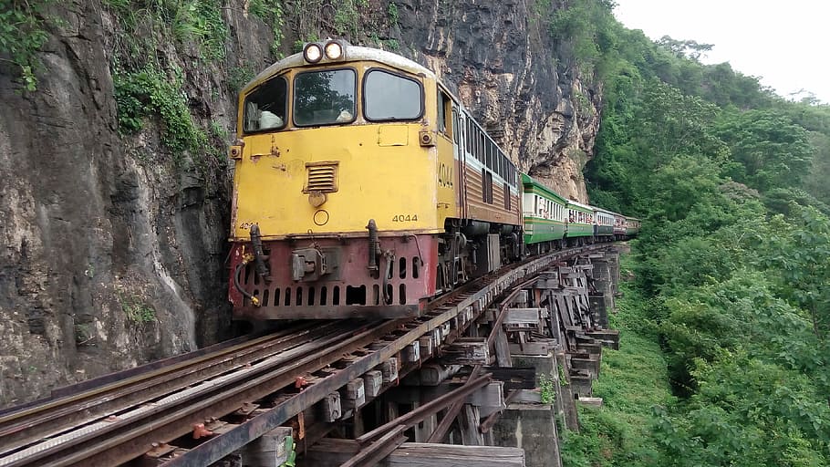 yellow train on rails by a mountainside cliff, Thailand, Kanchanaburi