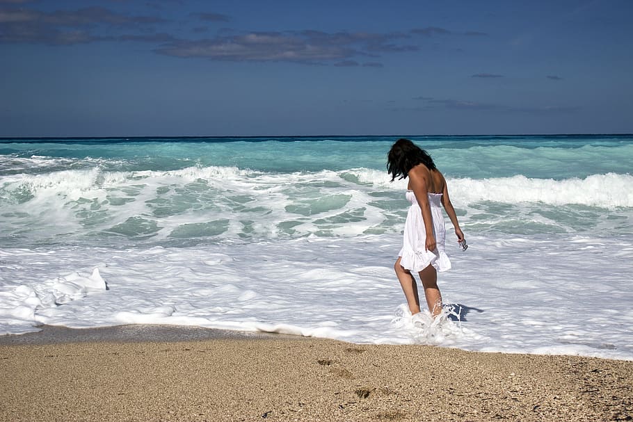 woman in white tube flare mini dress walking on seashore under blue sky during daytime