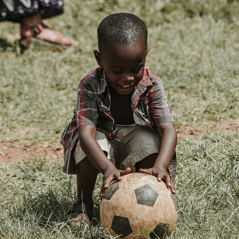 smiling boy sitting while holding soccer ball at daytime, boy holding white and black soccer ball