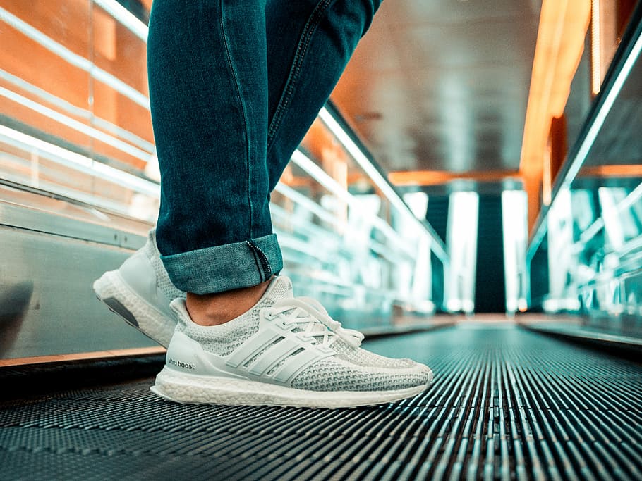 person standing on escalator wearing white adidas ultraBOOST running shoes