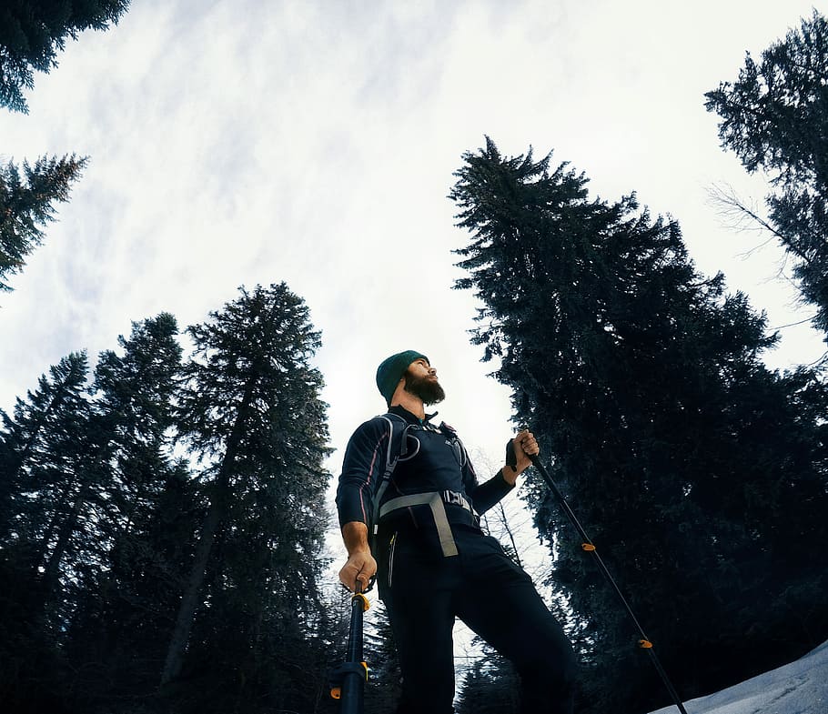man in forest, low-angle photography of man holding ski pole surrounded with trees