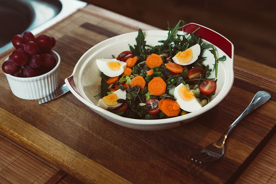 bowl of salad with slide of cooked egg with grapes on the side, bowl of egg salad beside fork and bread knife and bowl of grapes of tray HD wallpaper
