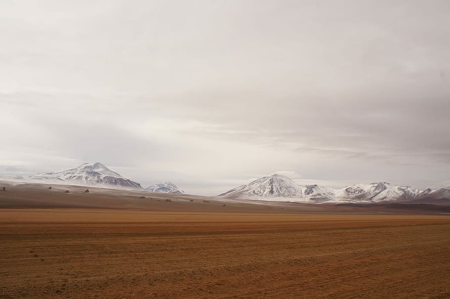 white mountains under gray sky during day, brown field near mountain at daytime HD wallpaper
