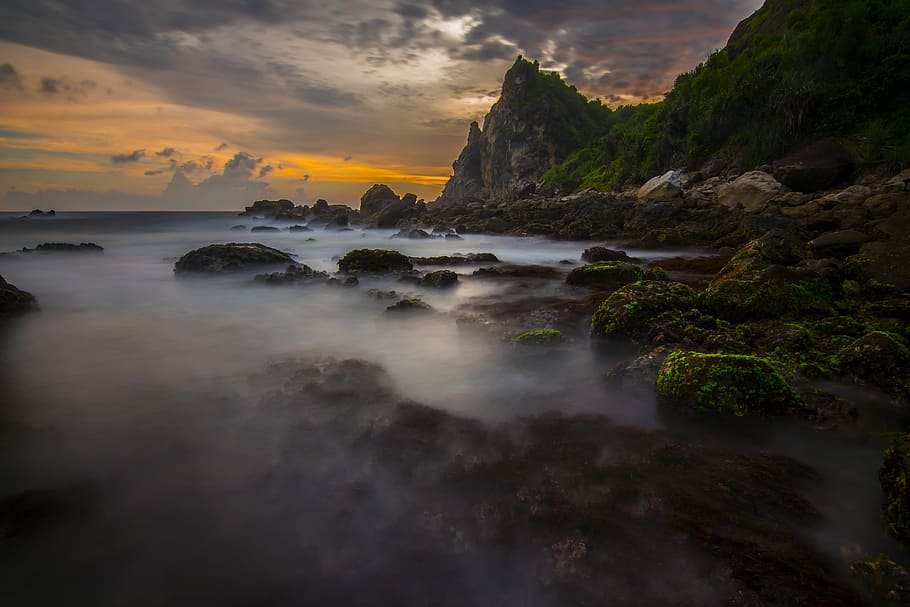 low angle photography of fog covered mountain, rock by the water under golden hour HD wallpaper