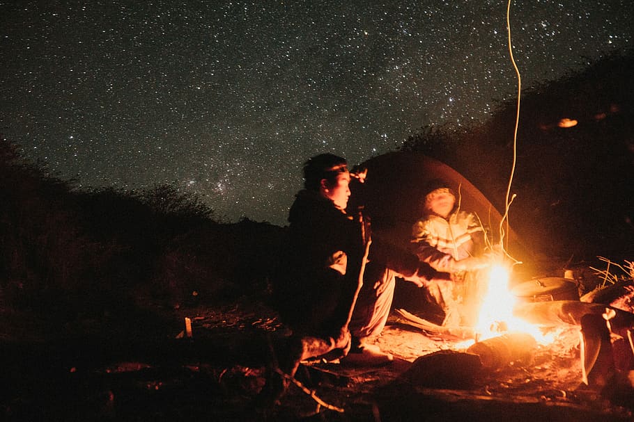 two persons lighting up campfier, two persons sitting near bonfire under starry night HD wallpaper